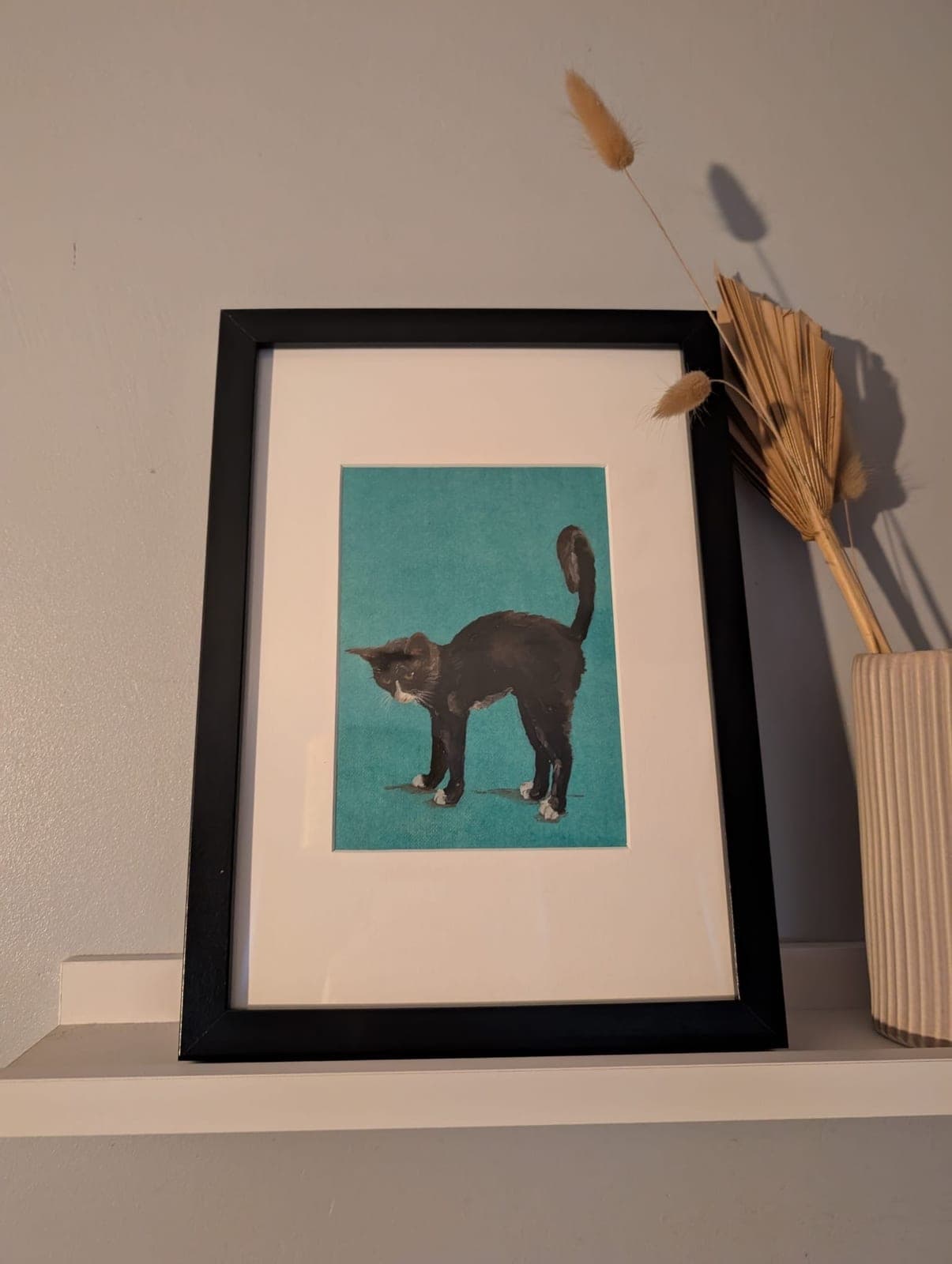 Mounted and framed, on a shelf beside dried grasses