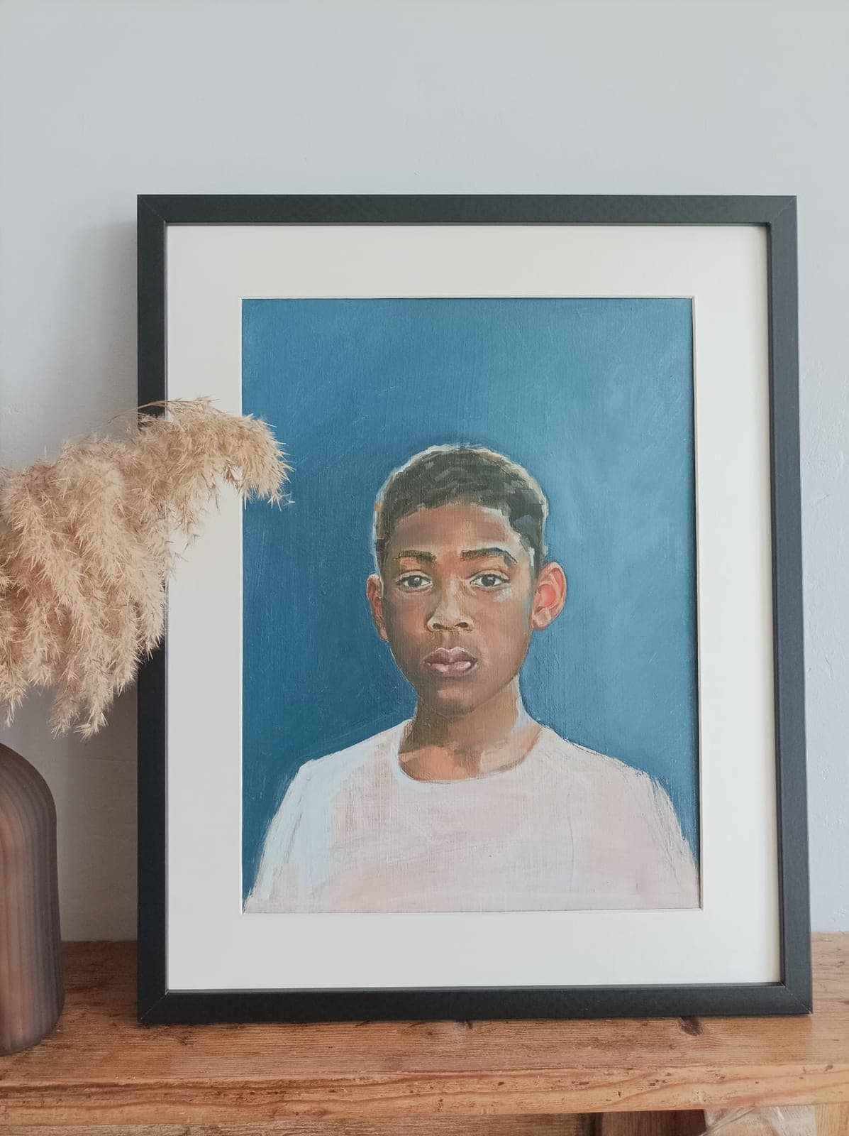 Framed, on a wooden sideboard beside dried grasses